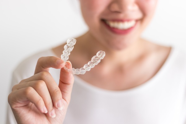 A smiling woman holding invisalign or invisible braces, orthodontic equipment